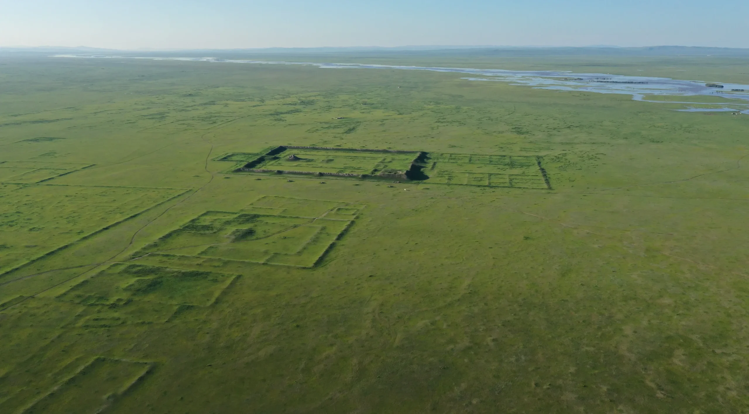 Bild, das Landschaft zeigt. In der Bildmitte sind die Ruinen einer rechteckigen Lehmmauer zu erkennen.